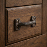 Angled view of rustic cast iron drawer pull with slotted screws on a wooden cabinet