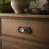 Ornate black cast iron backplate with clear glass drawer knob on a wood drawer