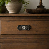 Straight-on view of black floral backplate and glass cabinet knob on a wooden drawer