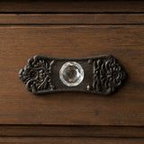 Close-up of faceted clear glass knob on ornate black cast iron drawer backplate