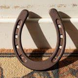 Rustic cast iron horseshoe good luck charm with nail holes, brown textured finish on cream backdrop
