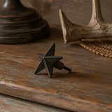 Black cast iron star cabinet knob with mounting screw on a rustic tabletop