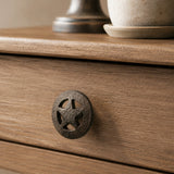 Close-up of textured black cast iron wagon wheel cabinet knob on a wood drawer