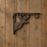 Front view of brown cast iron deer shelf bracket mounted on wood paneling