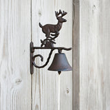 Cast iron deer head door bell mounted on weathered wood with decorative mounting bracket and hanging bell below