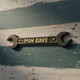 Cast iron Man Cave spanner wrench plaque with gold lettering on rustic wood backdrop