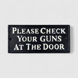 Black cast iron western saloon sign with cream text reading Please Check Your Guns at the Door