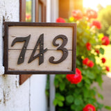 Vintage cast iron address numbers 743 on weathered wood base, garden setting with flowering plants