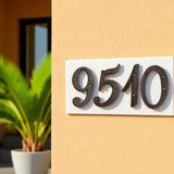 Antique cast iron house numbers 9510 on white wooden base, mounted on yellow stucco wall