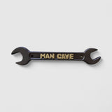 Black cast iron Man Cave wrench decor with embossed gold text on white background