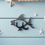 Black cast iron fish wall hook with detailed scales, double hooks, styled on striped nautical background