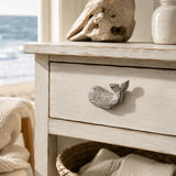 Close-up of white whale cabinet knob on a weathered cream drawer front