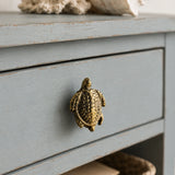 Close-up of brass sea turtle cabinet knob on a weathered blue drawer front