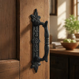 Black cast iron ornate door pull handle mounted on a rustic wood door