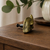 Side view of antique brass fox cabinet knob with mounting screw on wood tabletop