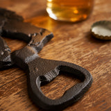 Black cast iron Bigfoot bottle opener beside beer bottle and caps, SKU GB78071