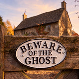 Cream and black cast iron Beware of the Ghost wall plaque mounted on a wooden gate, SKU GB78095