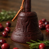 Close view of burgundy cast iron hand bell with textured finish and leather strap, SKU GB78097