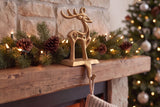 Champagne gold cast iron reindeer stocking holder on a rustic wood mantel with pine garland and a knit stocking