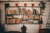Rustic bookshelf filled with books, with terracotta pots and trailing plants on a whitewashed plank wall