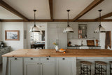 Modern farmhouse kitchen with wood ceiling beams, a butcher-block island, pendant lights and iron bar stools