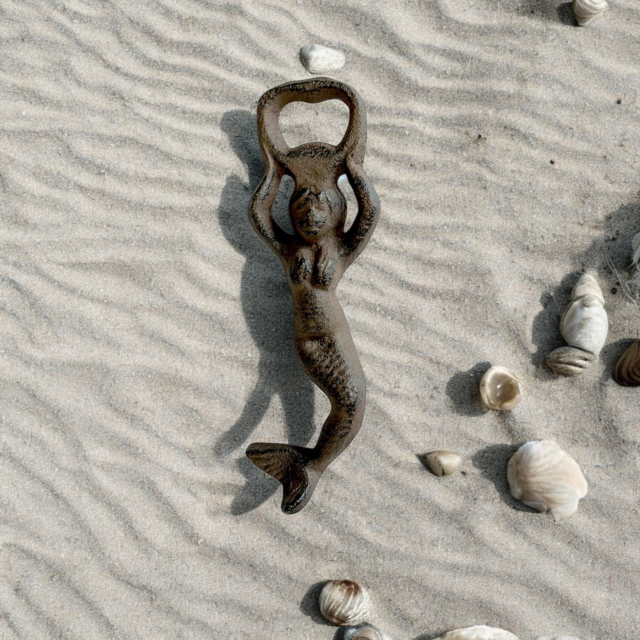 Rustic dark brown cast iron mermaid bottle opener displayed on sand with shells, nautical beach decor
