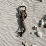 Rustic dark brown cast iron mermaid bottle opener displayed on sand with shells, nautical beach decor