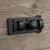 Black cast iron slide bolt latch on weathered wood background, rustic vintage door hardware