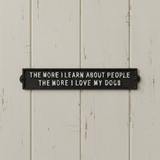 Black cast iron dog plaque mounted on white shiplap wall with text about loving dogs more than people