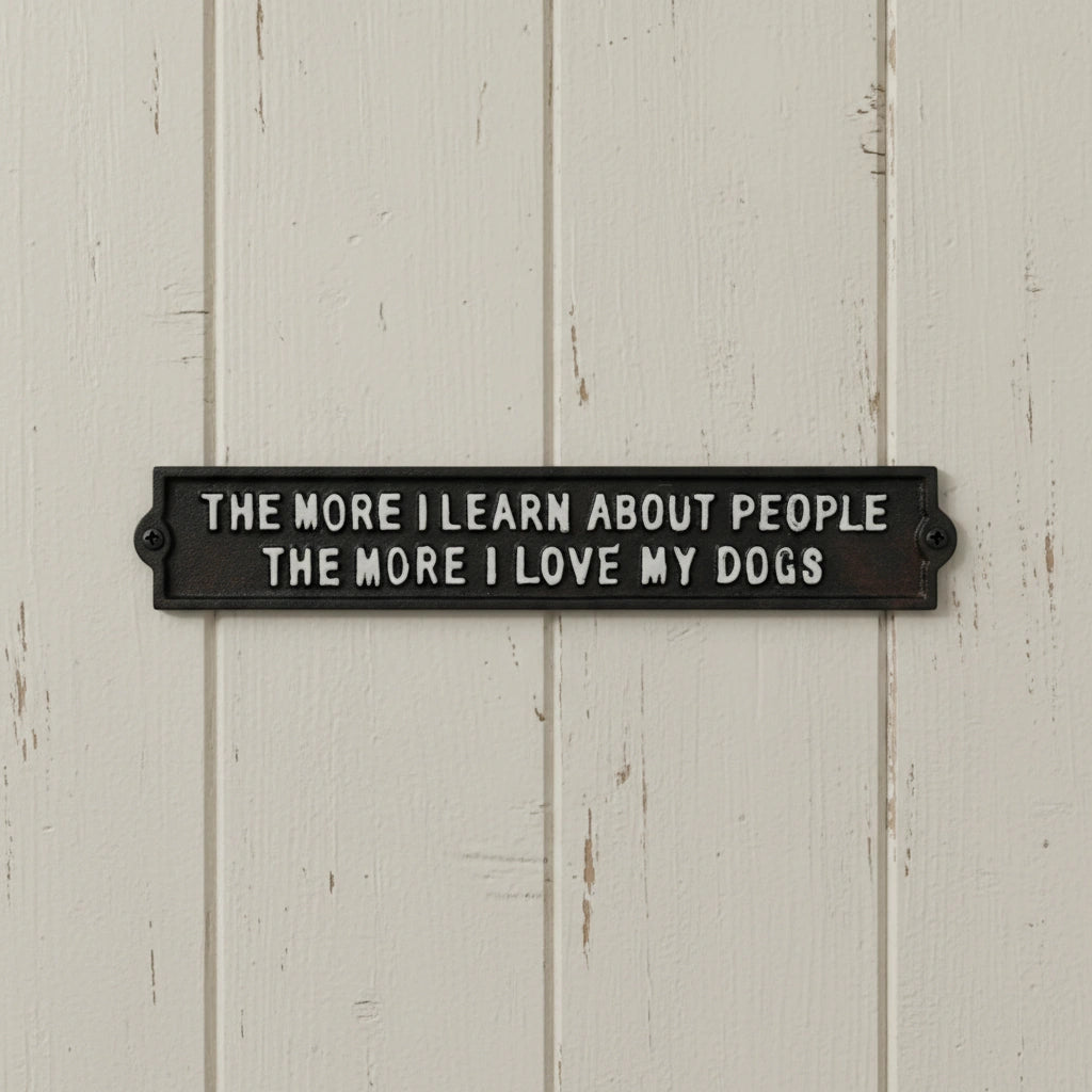 Black cast iron dog plaque mounted on white shiplap wall with text about loving dogs more than people