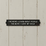 Black cast iron dog plaque mounted on white shiplap wall with text about loving dogs more than people