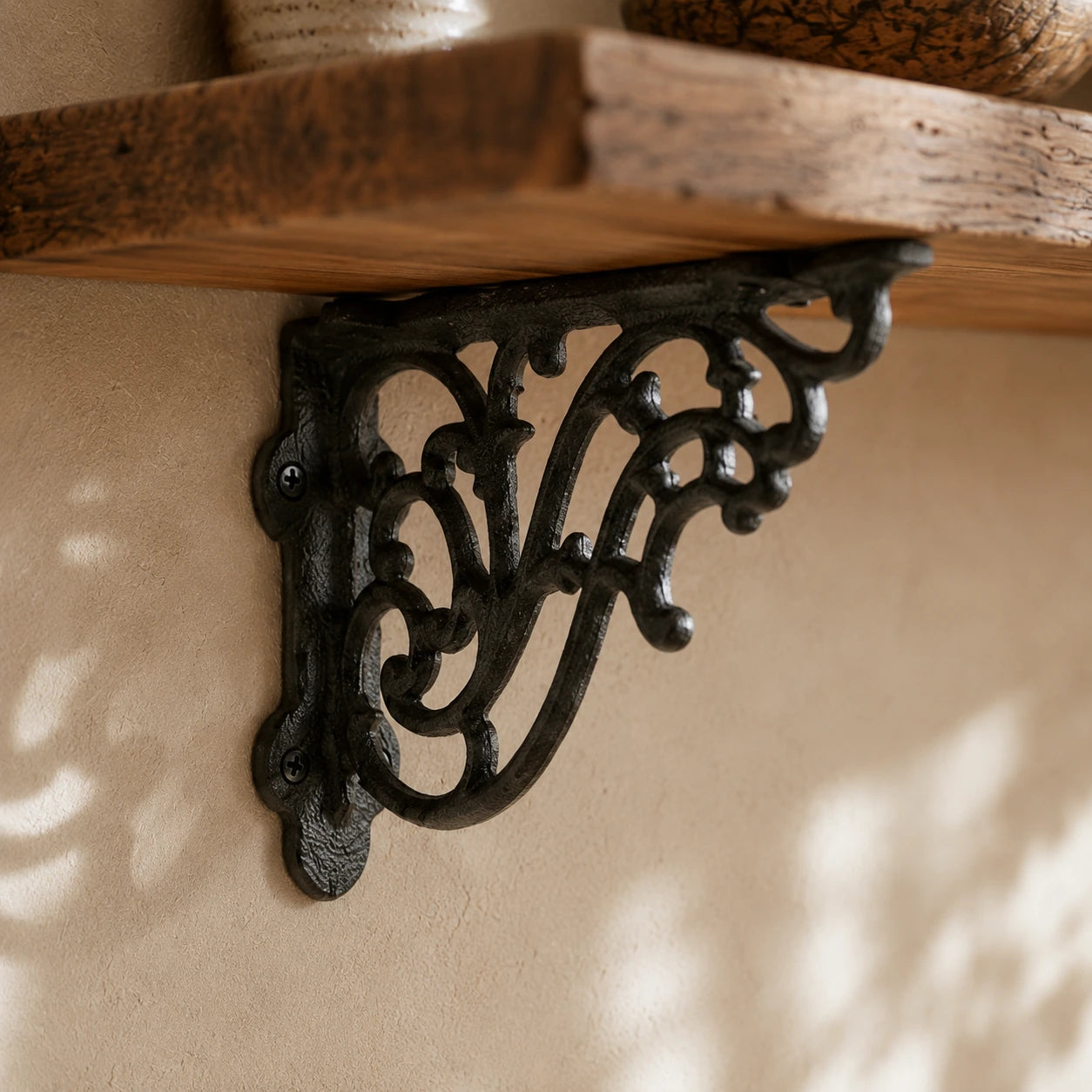 Black cast iron decorative shelf bracket supporting a rustic wood wall shelf