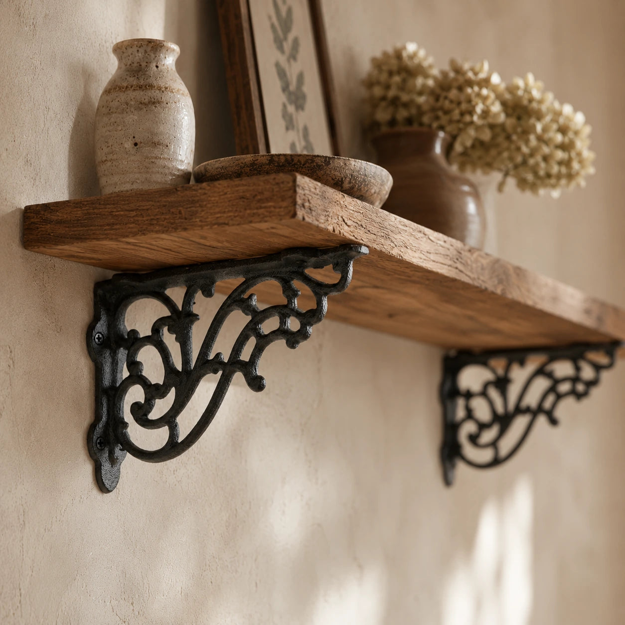 Angled view of ornate black cast iron shelf brackets under a wooden wall shelf