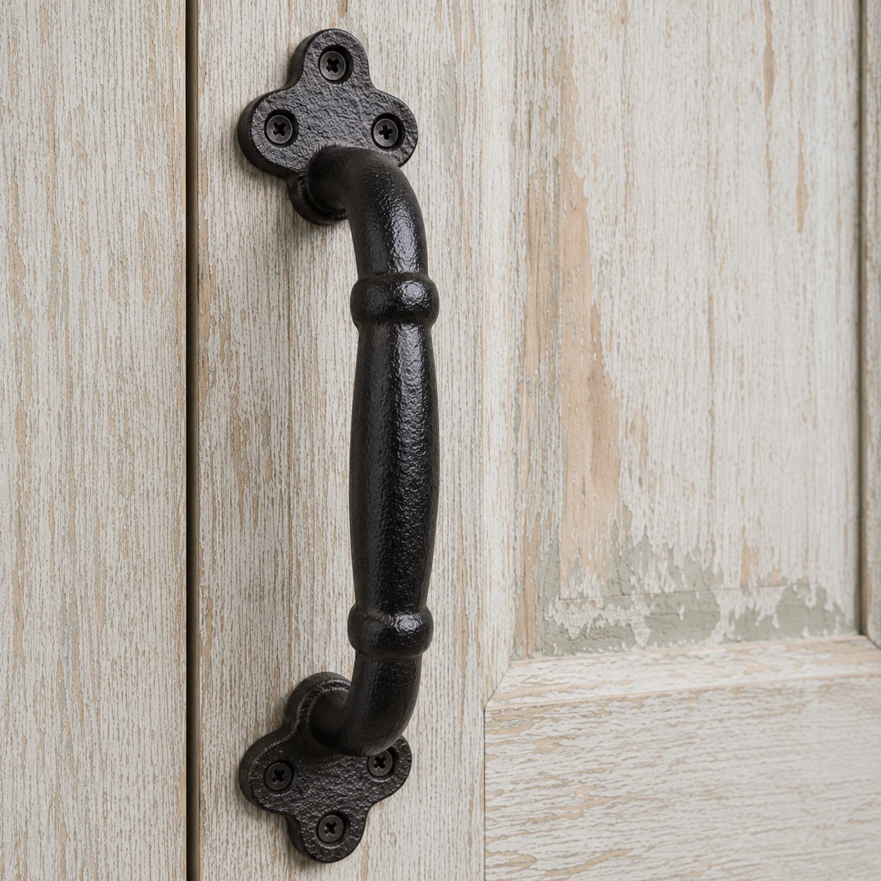 Close-up of black cast iron door pull handle with clover mounting plates and screws