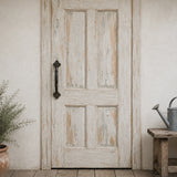 Distressed white wood door with black cast iron pull handle in a rustic entryway