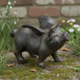 Black cast iron small flying pig figurine with wings in garden setting among white flowers