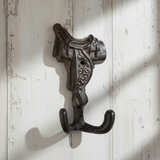 Cast iron horse saddle hook with ornate detailing and dual hooks, brown patina finish mounted on white shiplap