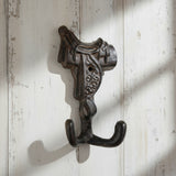 Cast iron horse saddle hook with ornate detailing and dual hooks, brown patina finish mounted on white shiplap