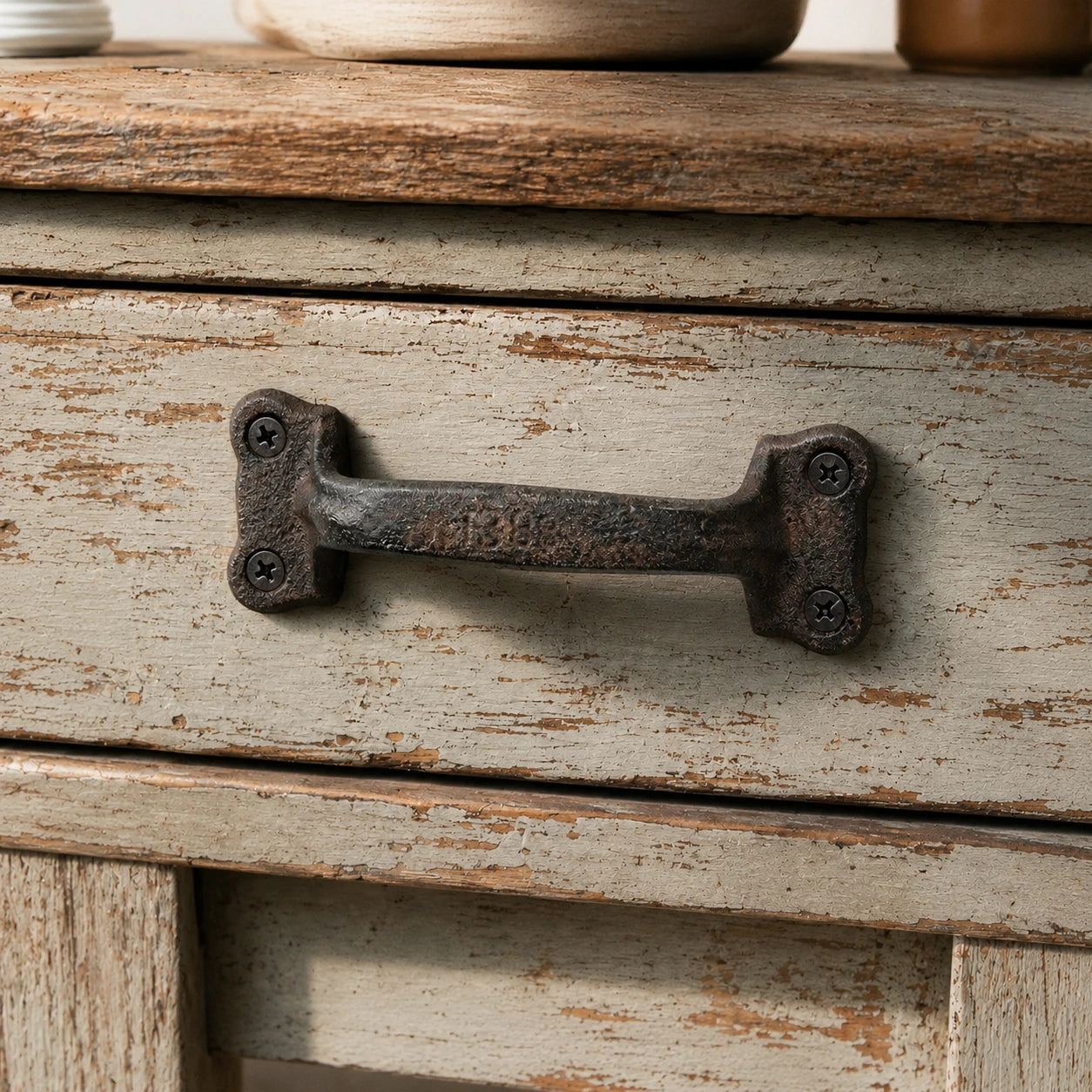 Close-up of cast iron cabinet handle with four black mounting screws