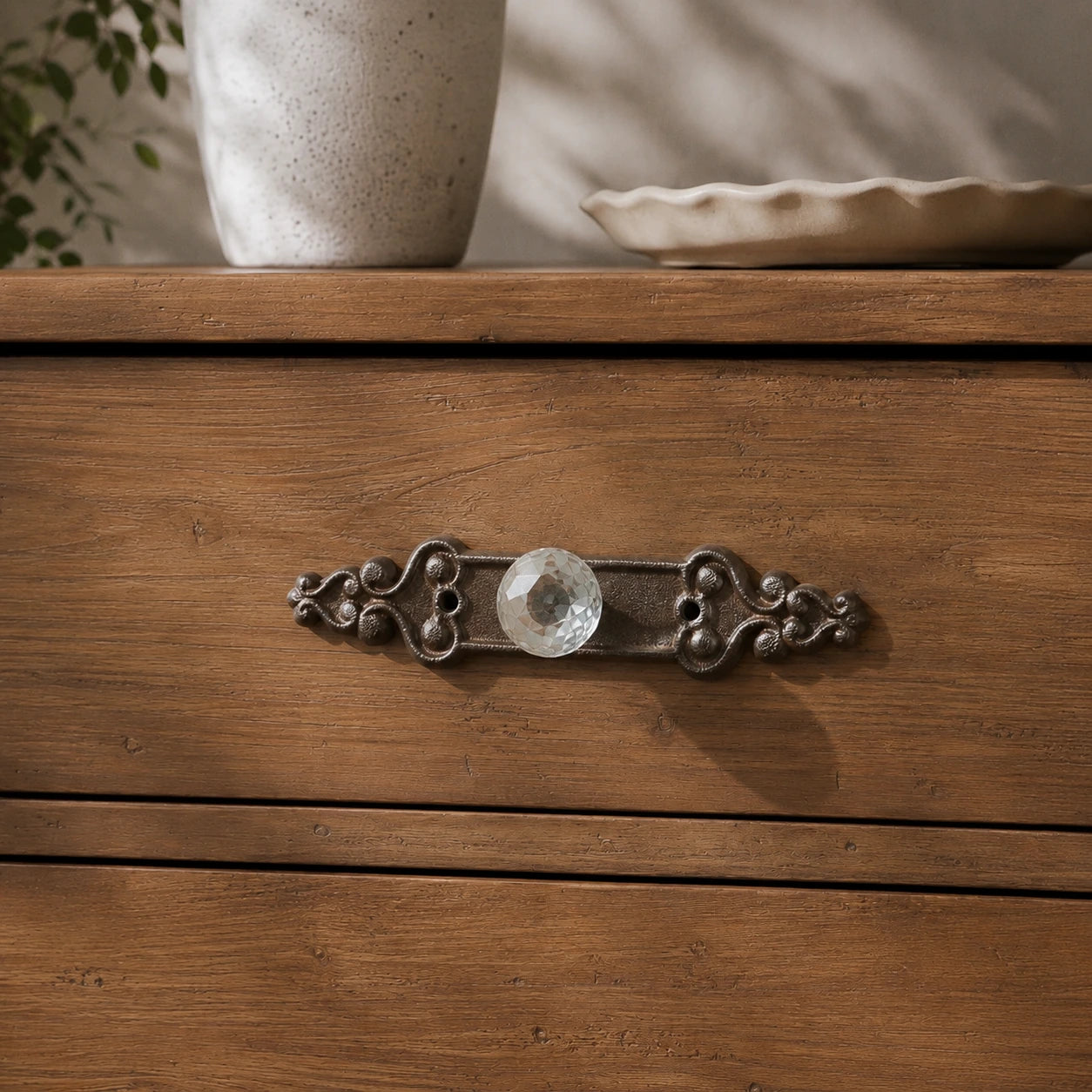 Straight-on view of ornate brown cast iron cabinet backplate with faceted glass knob