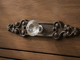 Close-up of faceted clear glass knob on antique brown cast iron scroll backplate