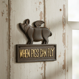 Cast iron flying pig plaque on whitewashed wood wall with brass When Pigs Can Fly text sign