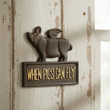 Cast iron flying pig plaque on whitewashed wood wall with brass When Pigs Can Fly text sign
