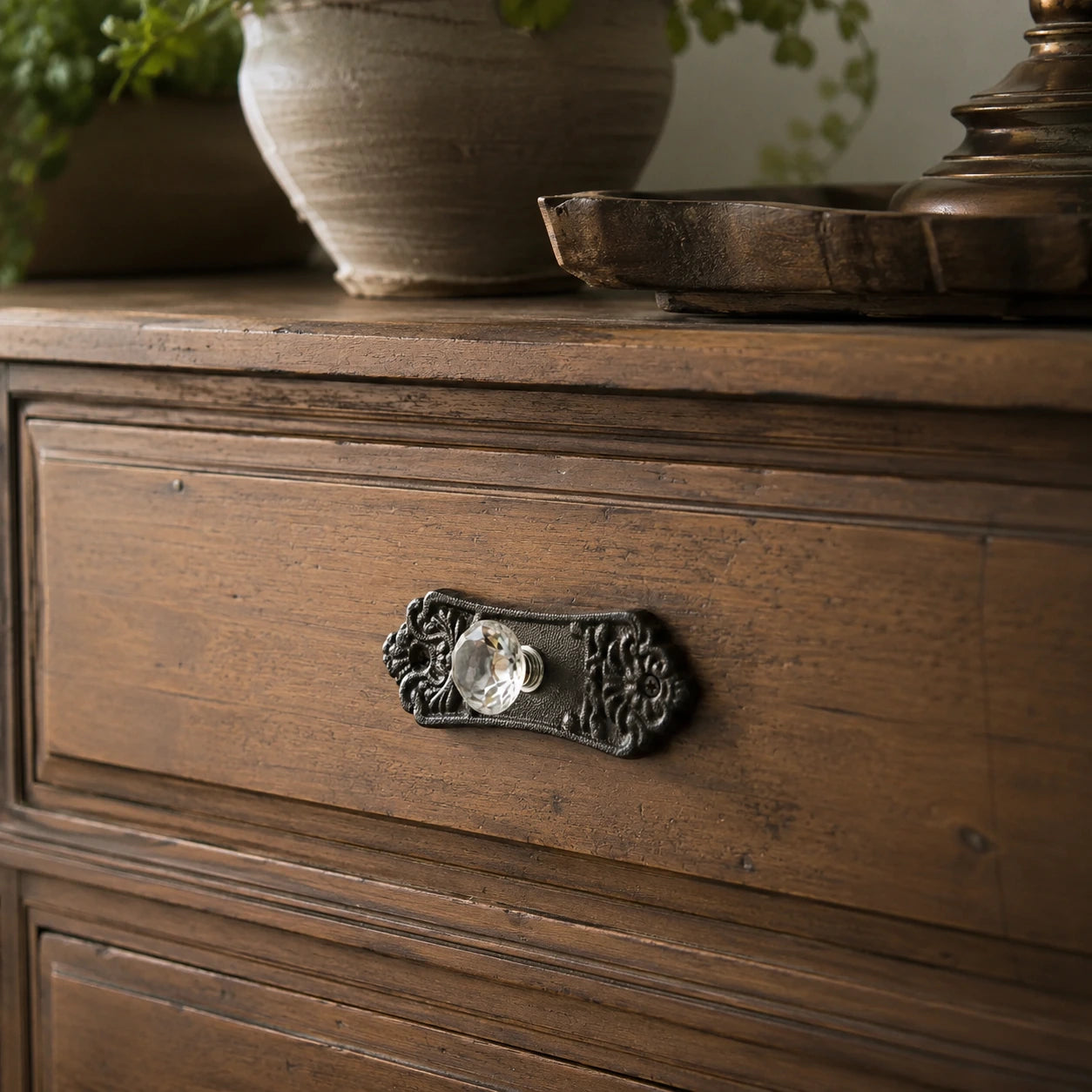 Ornate black cast iron backplate with clear glass drawer knob on a wood drawer
