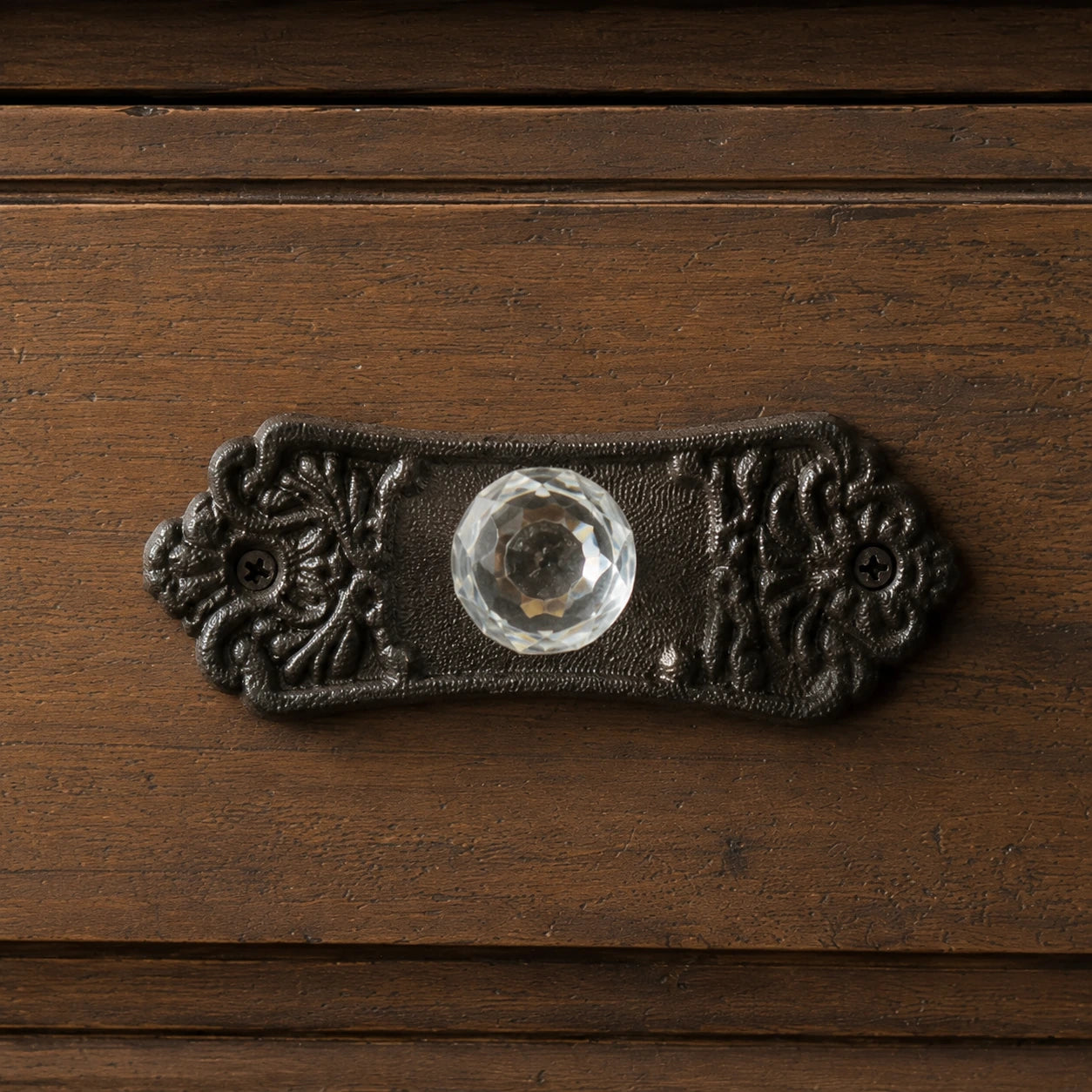 Close-up of faceted clear glass knob on ornate black cast iron drawer backplate