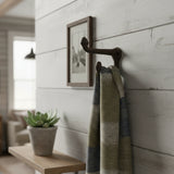 Towel hanging on a wall hook with a plant and framed picture in the background