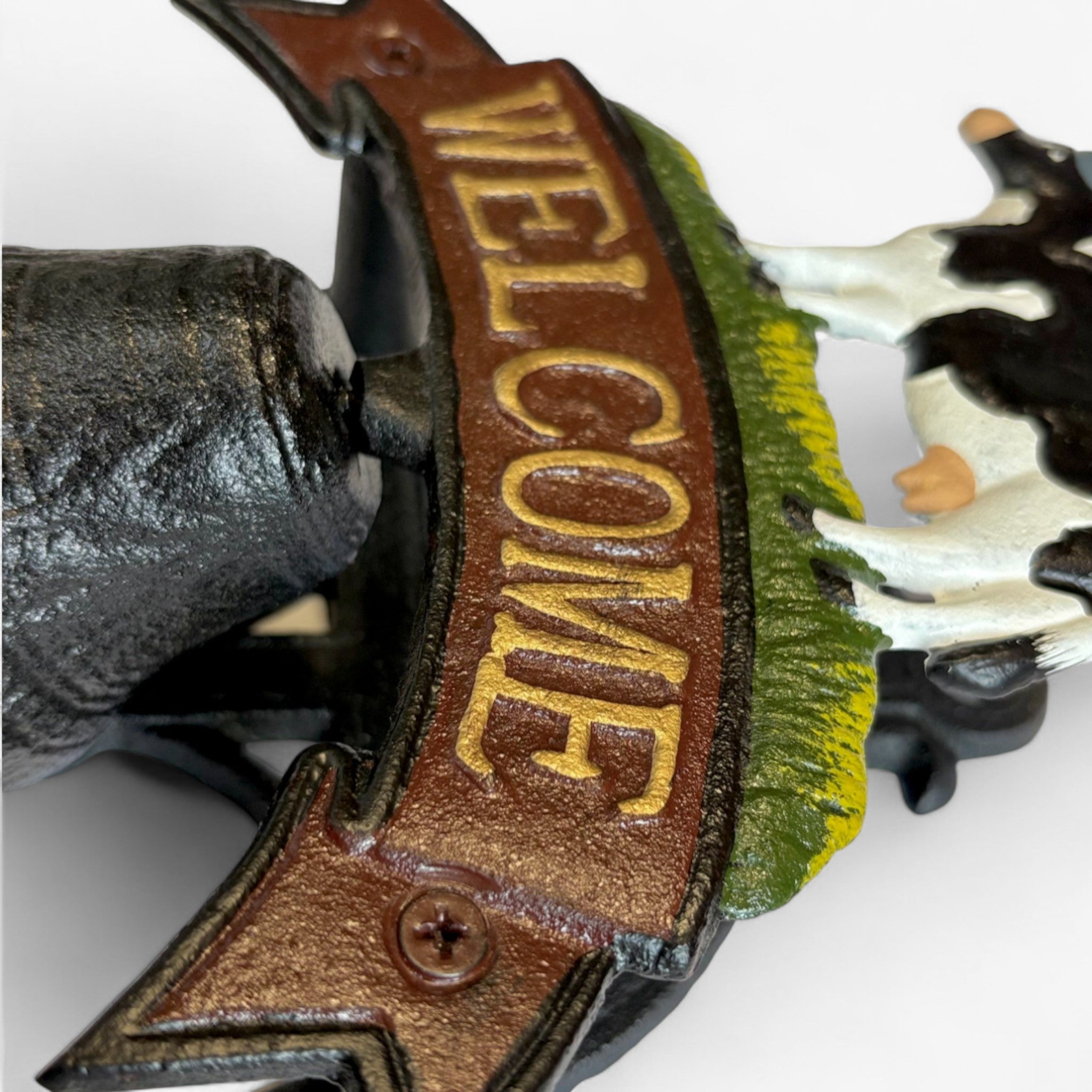 Close-up of brown leather welcome banner strap with brass lettering on cast iron cow sign