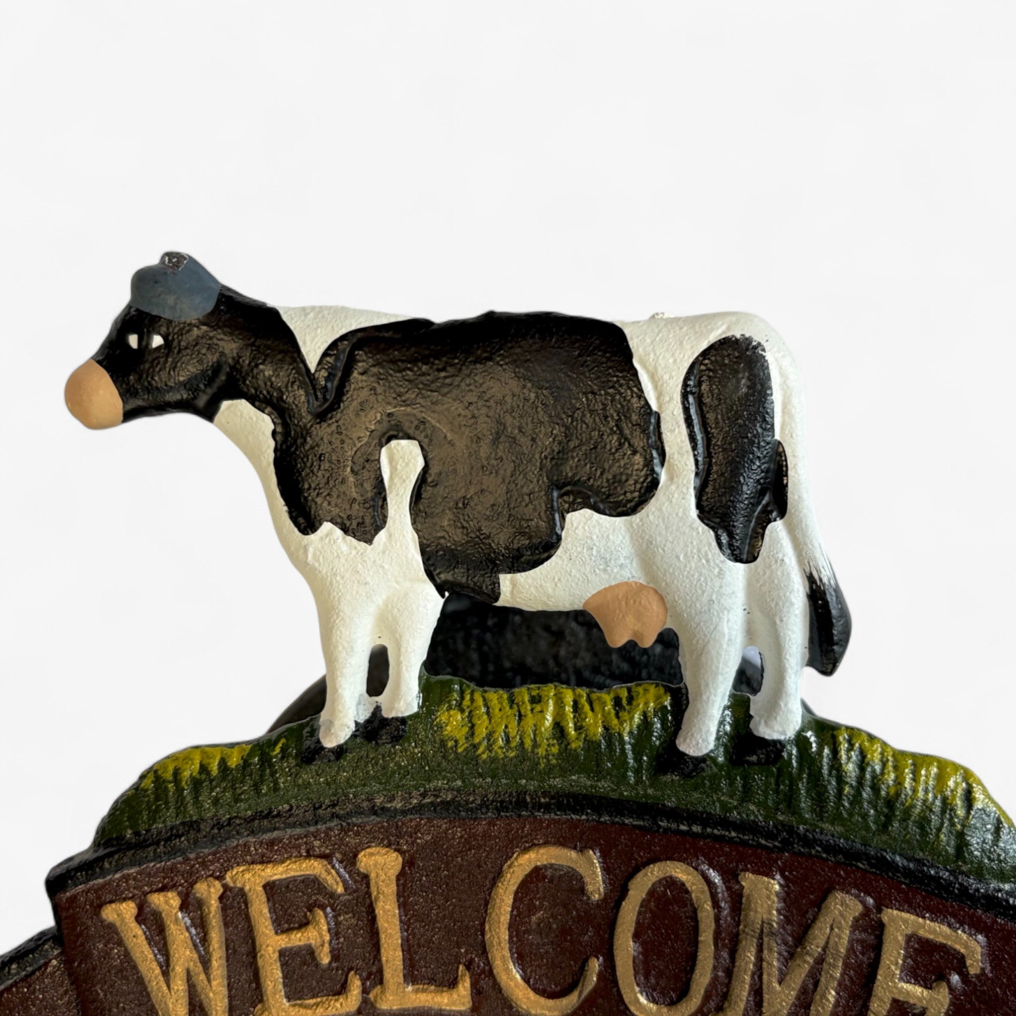 Black and white painted cast iron cow figurine with yellow grass base and brown welcome banner