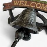 Cast iron bell detail with textured dark metal finish and brass welcome text banner above