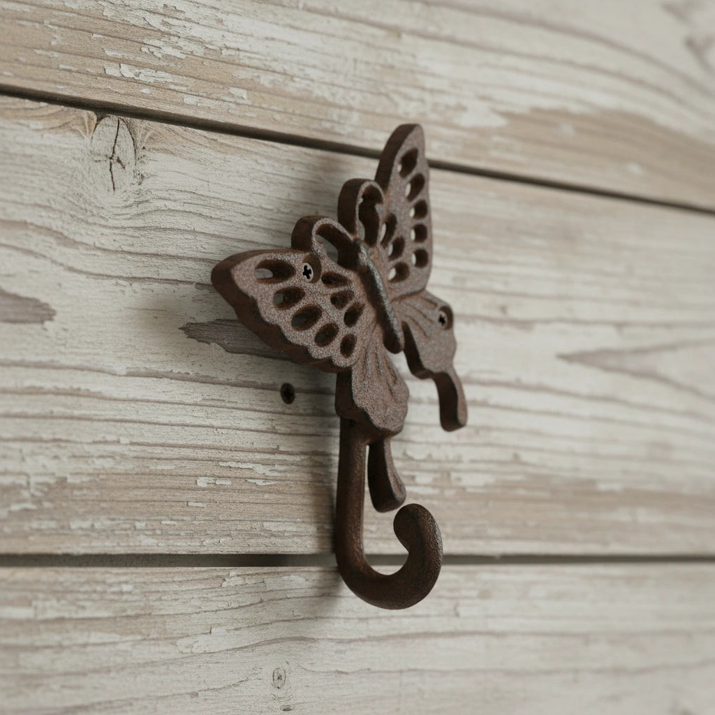 Cast iron butterfly wall hook with detailed wing cutouts and scrolled hook, rustic brown finish on whitewashed wood